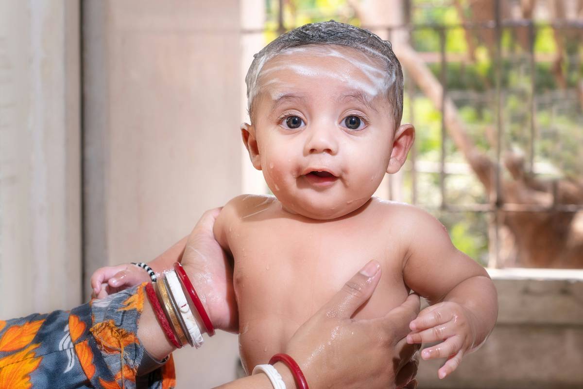 Mother applying green baby lotion to infant wearing organic cotton onesie